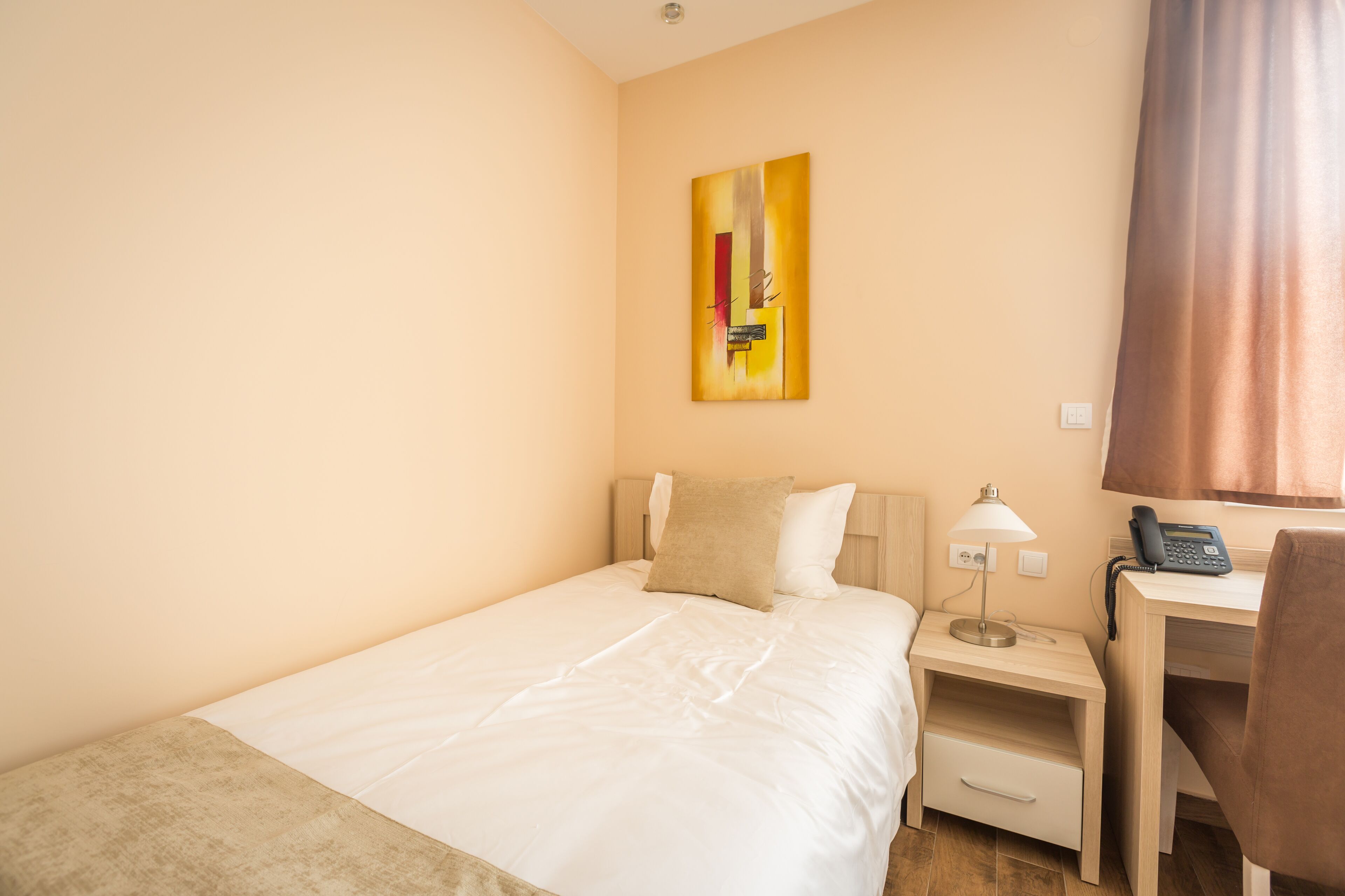 Ein Hotelzimmer mit Bett, Schreibtisch, Lampe, Telefon und einem Gemälde an der Wand.