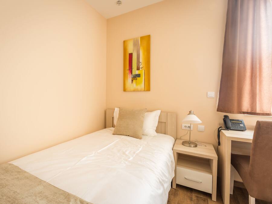 Ein Hotelzimmer mit Bett, Schreibtisch, Lampe, Telefon und einem Gemälde an der Wand.