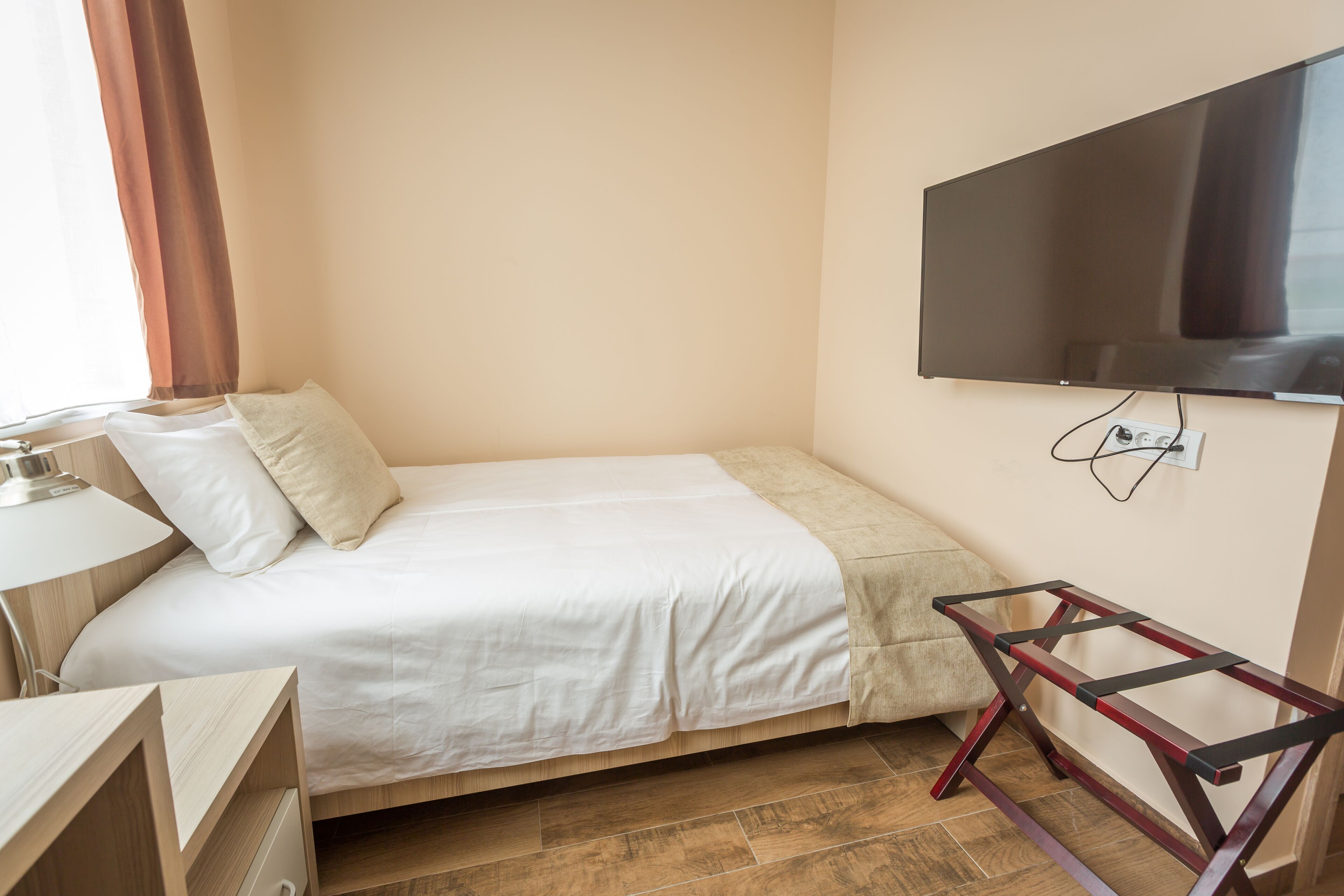 Une petite chambre à coucher, bien rangée, avec un lit, un bureau, une chaise et un téléviseur fixé au mur.