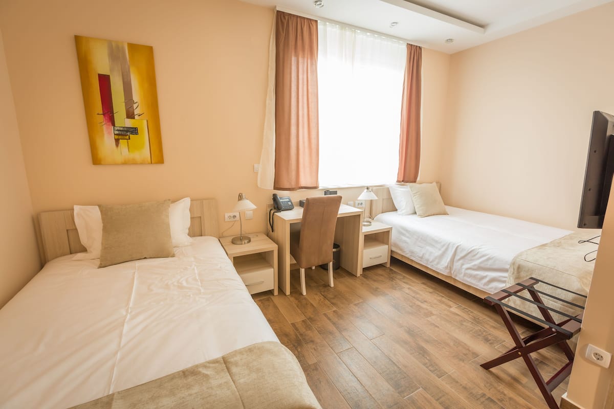 A hotel room with two beds, a desk, a chair, a TV, and a painting on the wall.