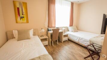 A hotel room with two beds, a desk, a chair, a TV, and a painting on the wall.
