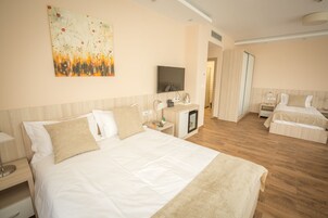 A hotel room with a large bed, a bedside table, a TV, and a painting on the wall.