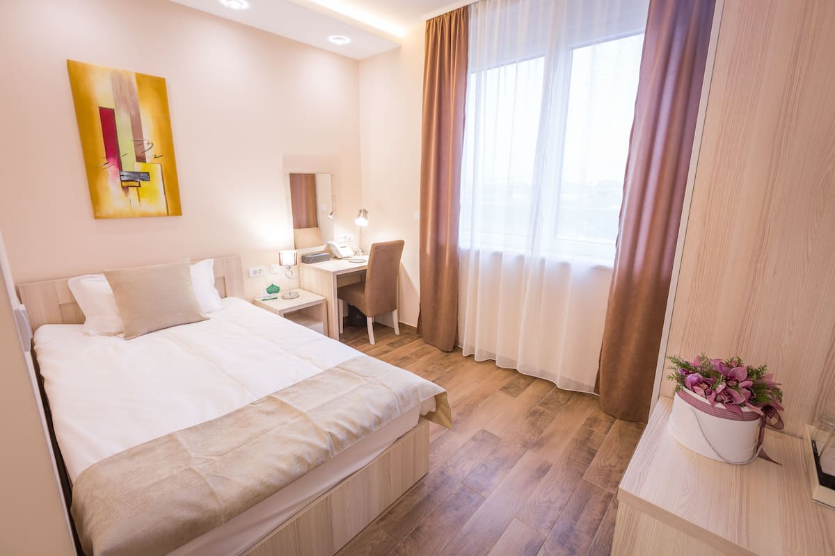 A hotel room with a bed, desk, chair, and a window with curtains.