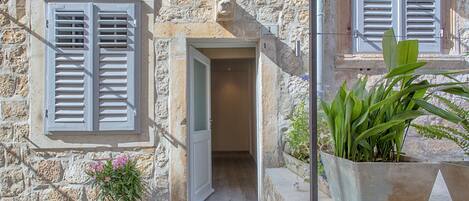 Un edificio de piedra con una puerta, una ventana con contraventanas y una planta en maceta.