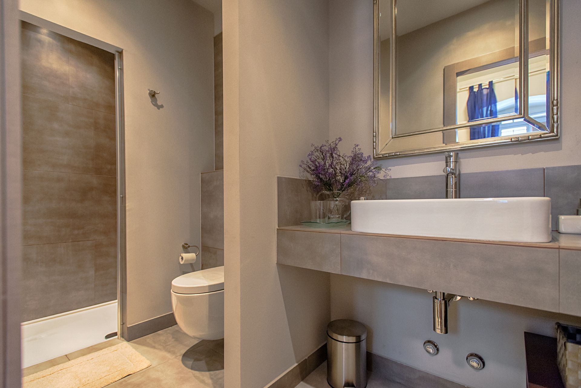A modern bathroom with a toilet, sink, mirror, and shower.