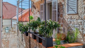 Een gebouw van steen met een rode dakbedekking, een balkon met plantenpotten en een metalen luifel.