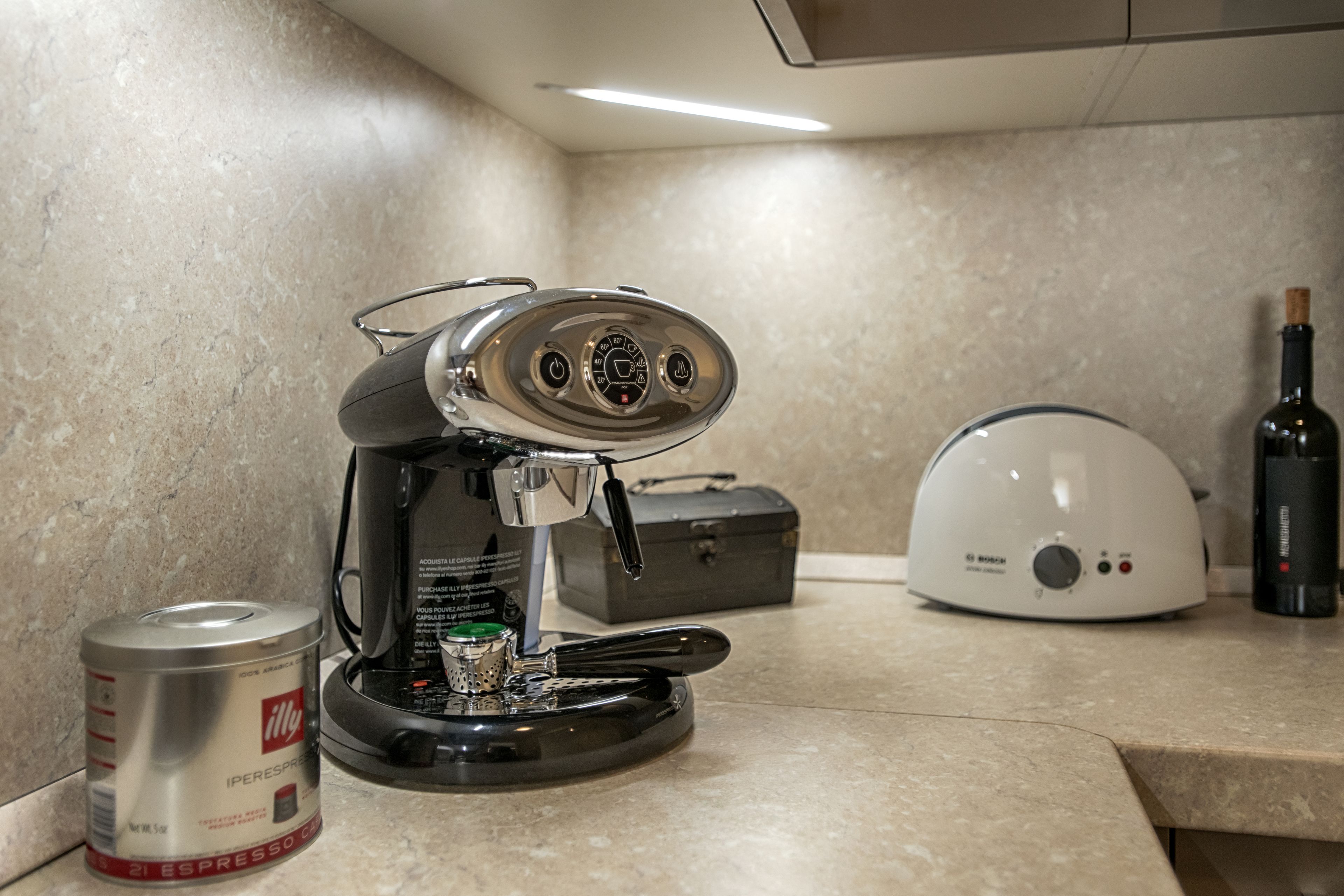 A coffee machine, a can of Iperespresso, and a bottle of wine on a kitchen counter.