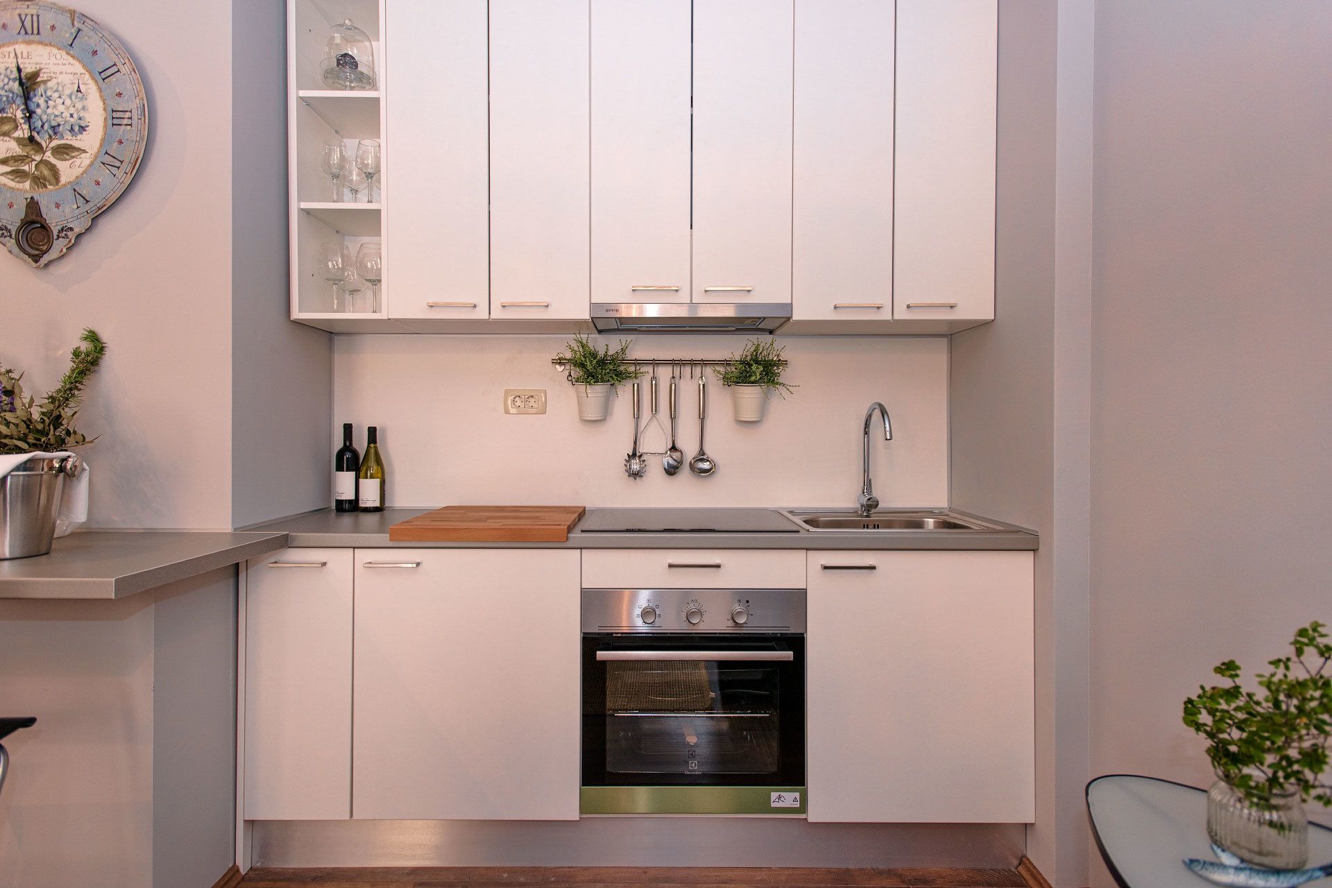 Eine moderne Küche mit wei ßen Schränken, einem Edelstahlbackofen und einer Uhr an der Wand.