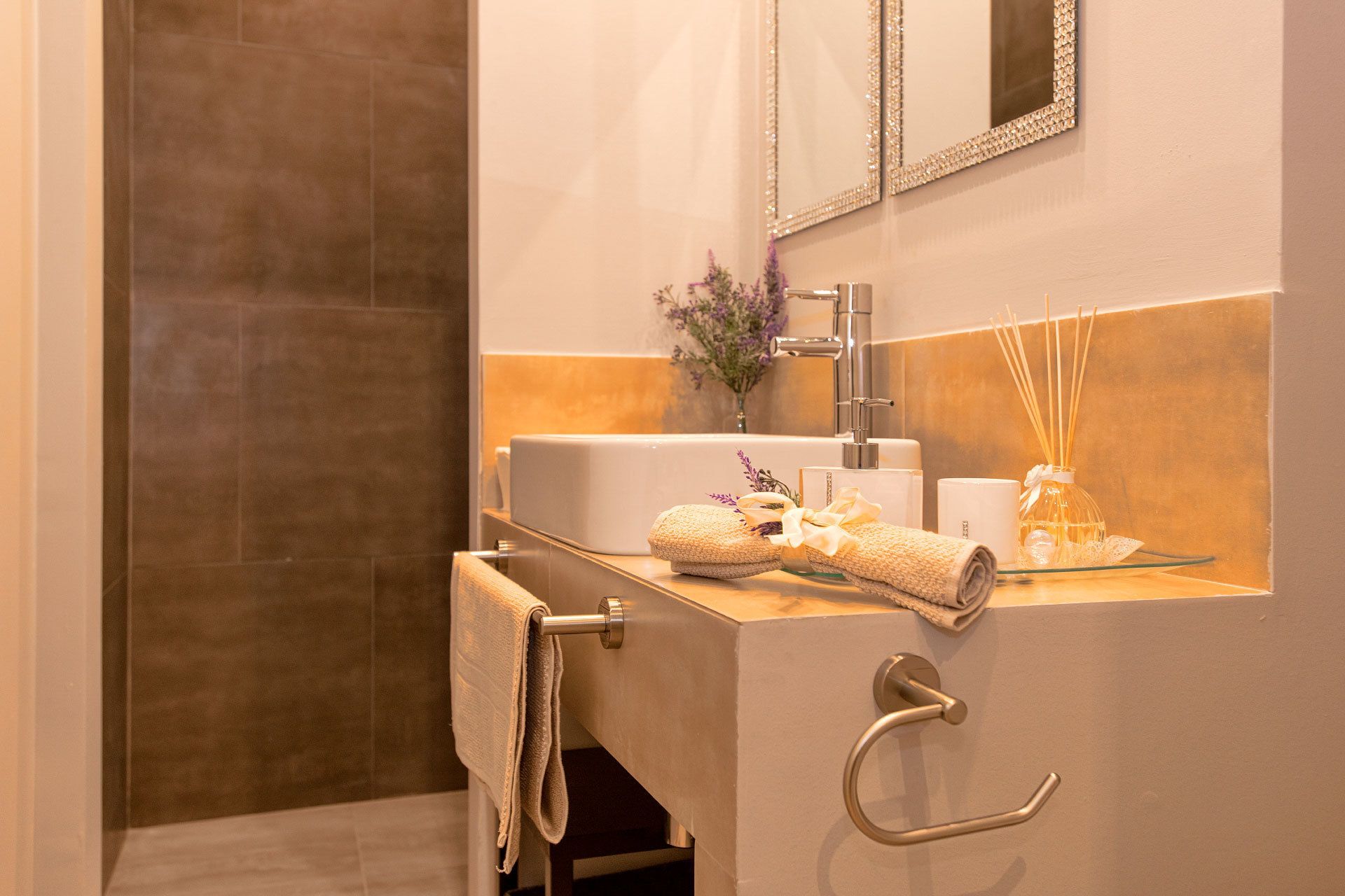 Un baño con lavamanos, espejo, toallero y un florero decorativo con cañas.