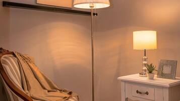 A bedroom with a bed, a chair, a bedside table with a lamp, and a framed picture on the wall.