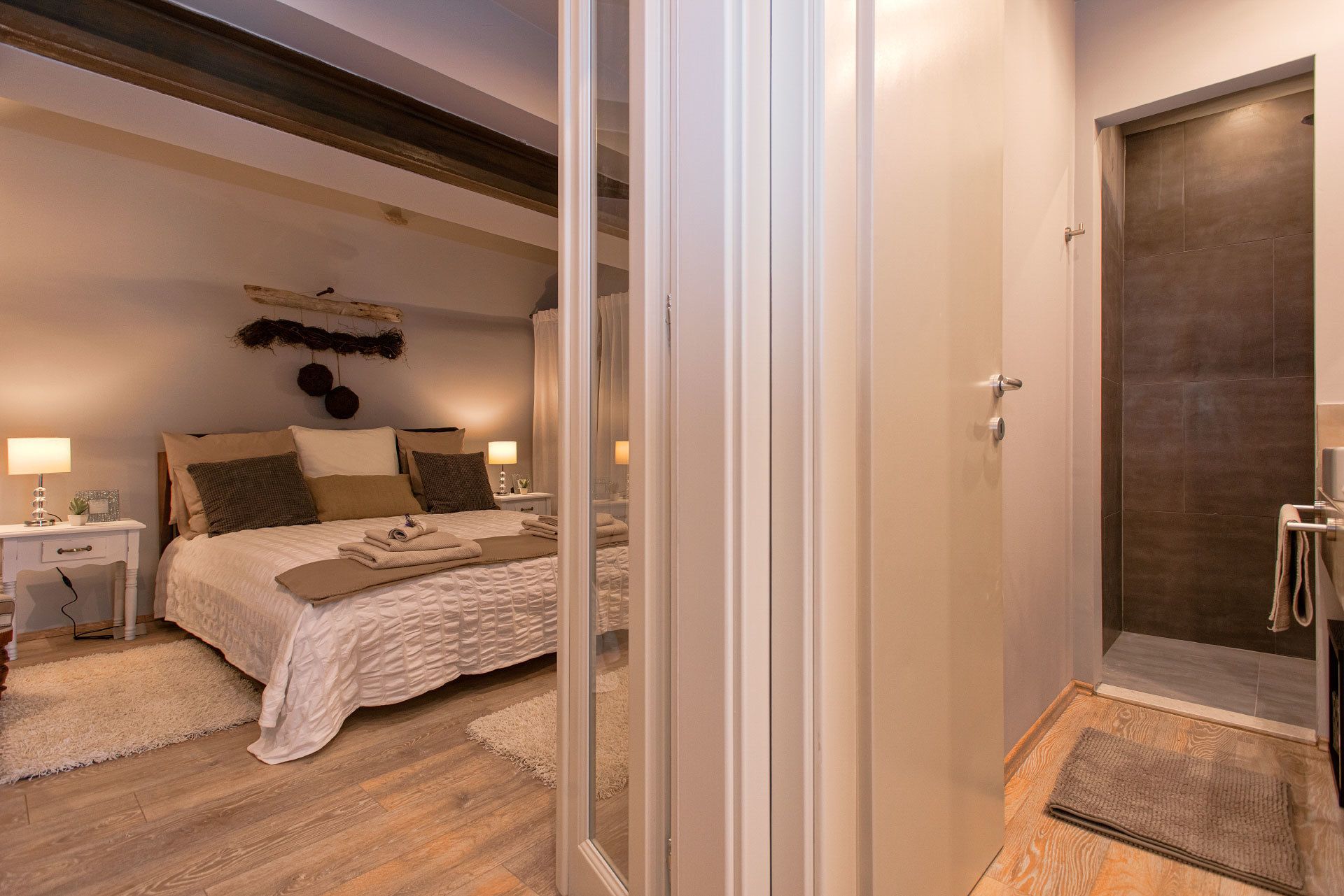 Un dormitorio con cama, mesitas de noche, lámpara, espejo y una puerta que da a un baño.