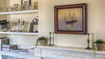A room with a fireplace, a framed painting of a sailboat, and shelves with various items.