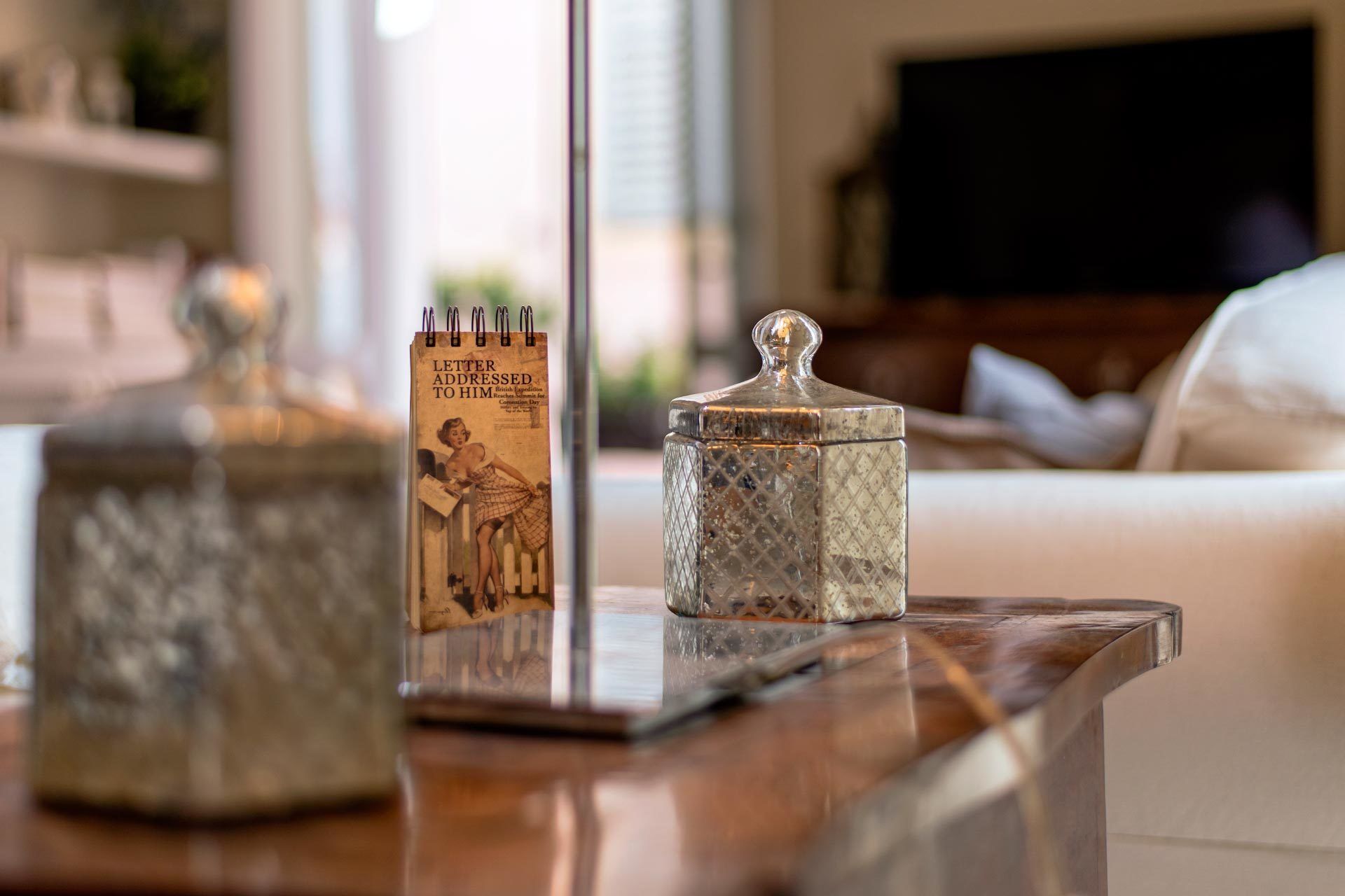 A wooden coffee table with a vintage letter addressed to a British expedition, a decorative glass jar, and a modern sofa in the background.