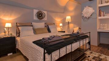 Un dormitorio ordenado con cama, mesitas de noche, lámparas, una estantería y decoración en la pared.