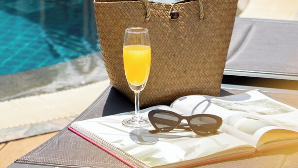 A poolside setting with a lounge chair, a woven tote bag, a glass of orange juice, sunglasses, and an open magazine. - Urbanite Hotel (Vientiane)