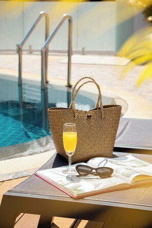 A poolside setting with a lounge chair, a woven tote bag, a glass of orange juice, sunglasses, and an open magazine. - Urbanite Hotel (Vientiane)
