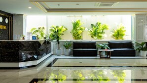 A hotel reception area with a black marble counter, a black sofa, and several potted plants. - Urbanite Hotel (Vientiane)