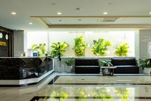 Zona de recepción de un hotel con un mostrador de mármol negro, un sofá negro y varias plantas en macetas.