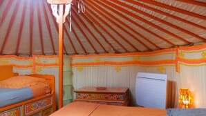 A room with a bed, a chest of drawers, a desk, and a hanging lamp. - Yourte Mongole (Huriel)