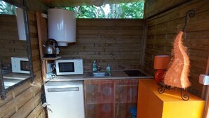 A compact kitchen with a microwave, kettle, sink, and a small refrigerator. - Yourte Mongole (Huriel)