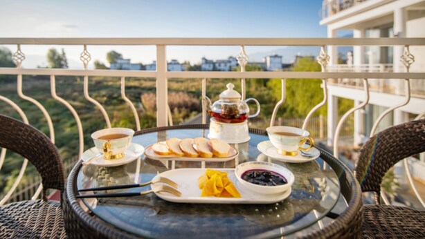 A table set with tea, coffee, bread, and fruit on a balcony with a scenic view. - Meili Xiangyue Villa Verde (Dali)