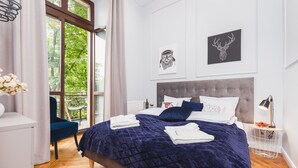 A modern bedroom with a large bed, a view of greenery outside, and artwork on the walls. - The Old Town View (Kraków)