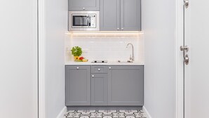 A compact kitchen with grey cabinets, a built-in microwave, a sink, and a small countertop with a plant and fruits. - The Old Town View (Kraków)