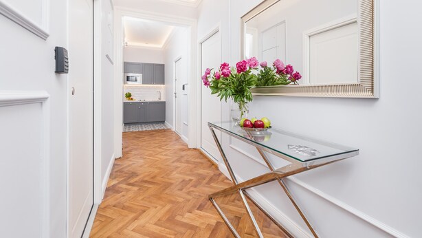 A hallway with a wooden floor, a glass console table with a vase of flowers, and a mirror on the wall. - The Old Town View (Kraków)