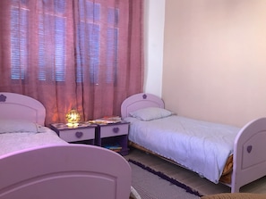 Une chambre avec deux lits, une table de chevet avec une lampe et une fenêtre avec des rideaux.