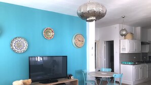 A living room with a TV, a dining table, and chairs. There is a kitchen area with cabinets and a sink. - Cosy Marsa Plage (La Marsa)