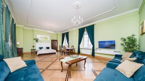 A hotel room with a large bed, a dining area, a TV, and a living area with blue sofas. - Apartamenty w Pałacu Pod Baranami (Kraków)