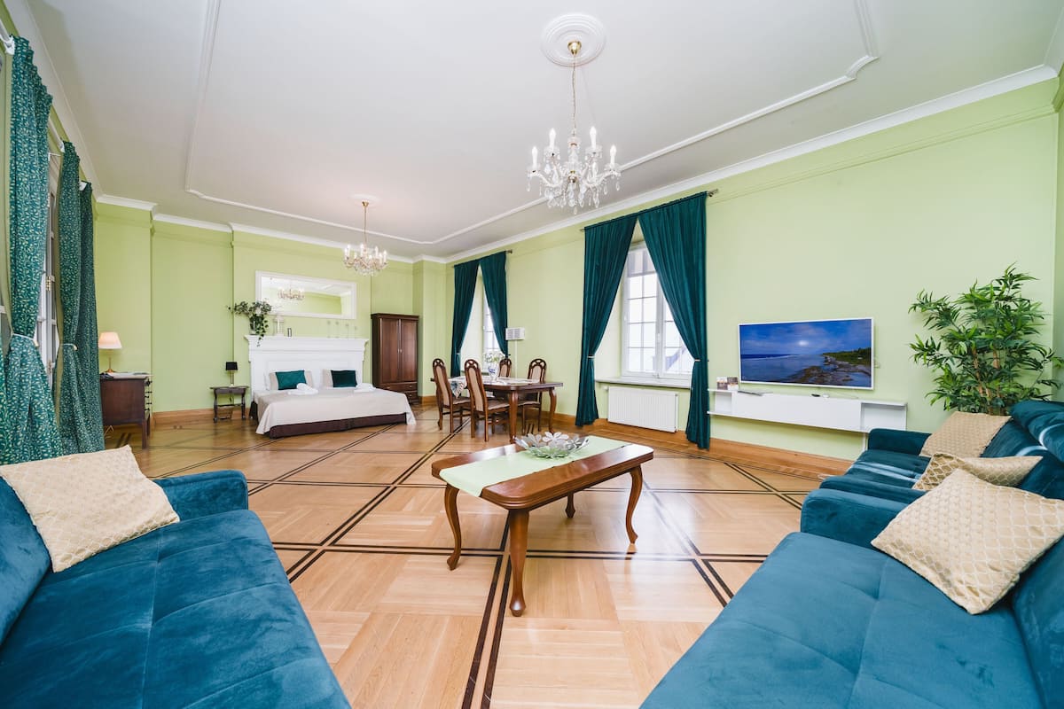 Hotelkamer met een groot bed, een eethoek, een televisie en een zithoek met blauwe banken.
