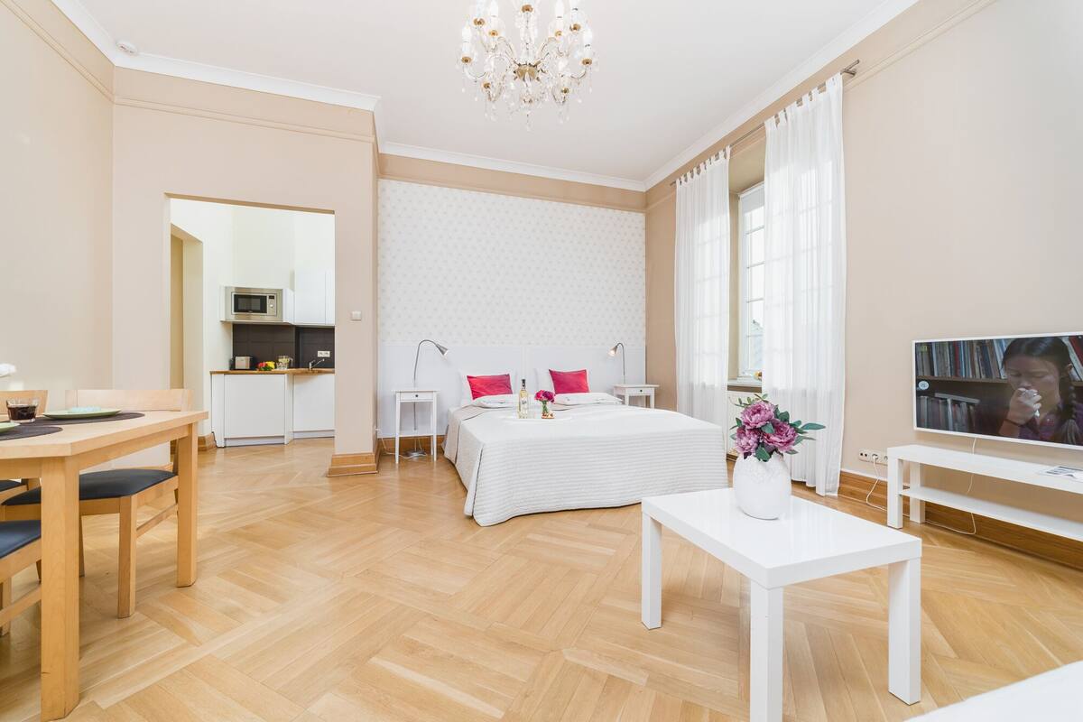 Een moderne hotelkamer met houten vloer, een bed met witte beddengoed, een klein nachtkastje, een televisie en een zithoek met een tafel en stoelen.