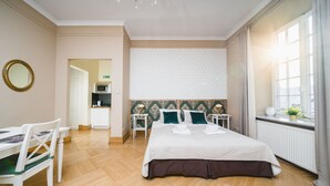 A hotel room with a bed, a desk, a chair, a small kitchenette, and a window with curtains. - Apartamenty w Pałacu Pod Baranami (Kraków)