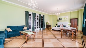 A room with a blue sofa, a wooden dining table with chairs, a chandelier, and a fireplace. - Apartamenty w Pałacu Pod Baranami (Kraków)
