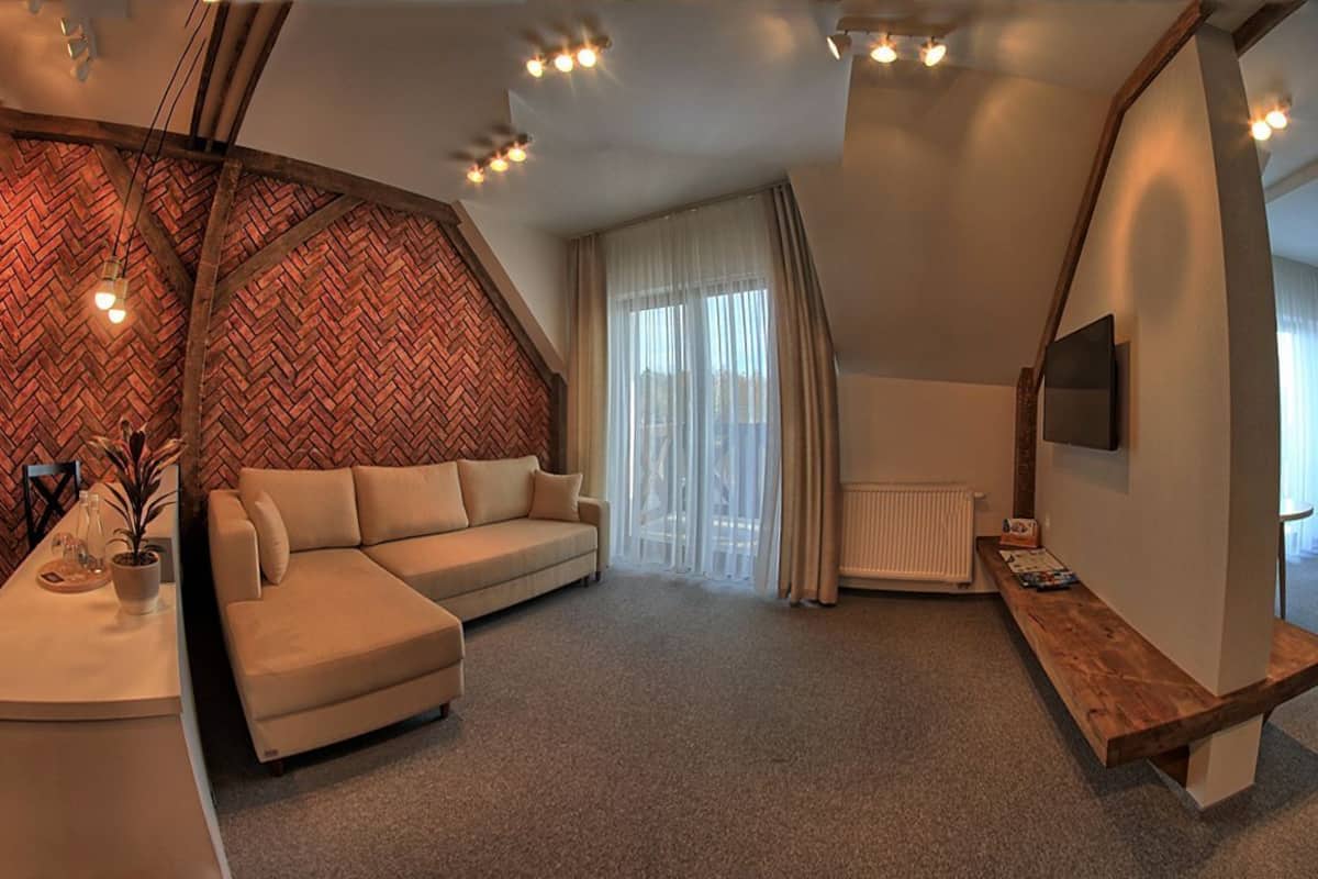 Una habitación de hotel moderna con pared de patrón espiga, un sofá, un banco de madera, una cama y un televisor montado en la pared.