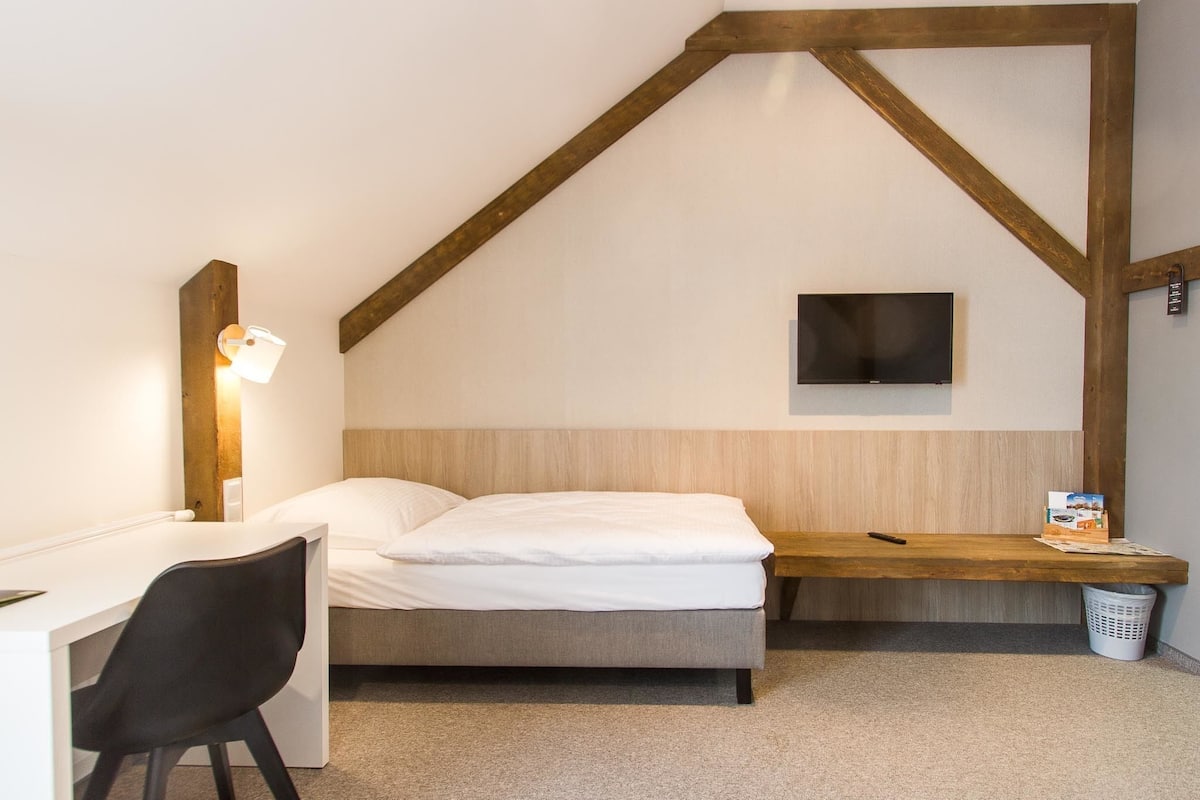 Un dormitorio con cama, escritorio, silla, televisor y cesto de ropa.