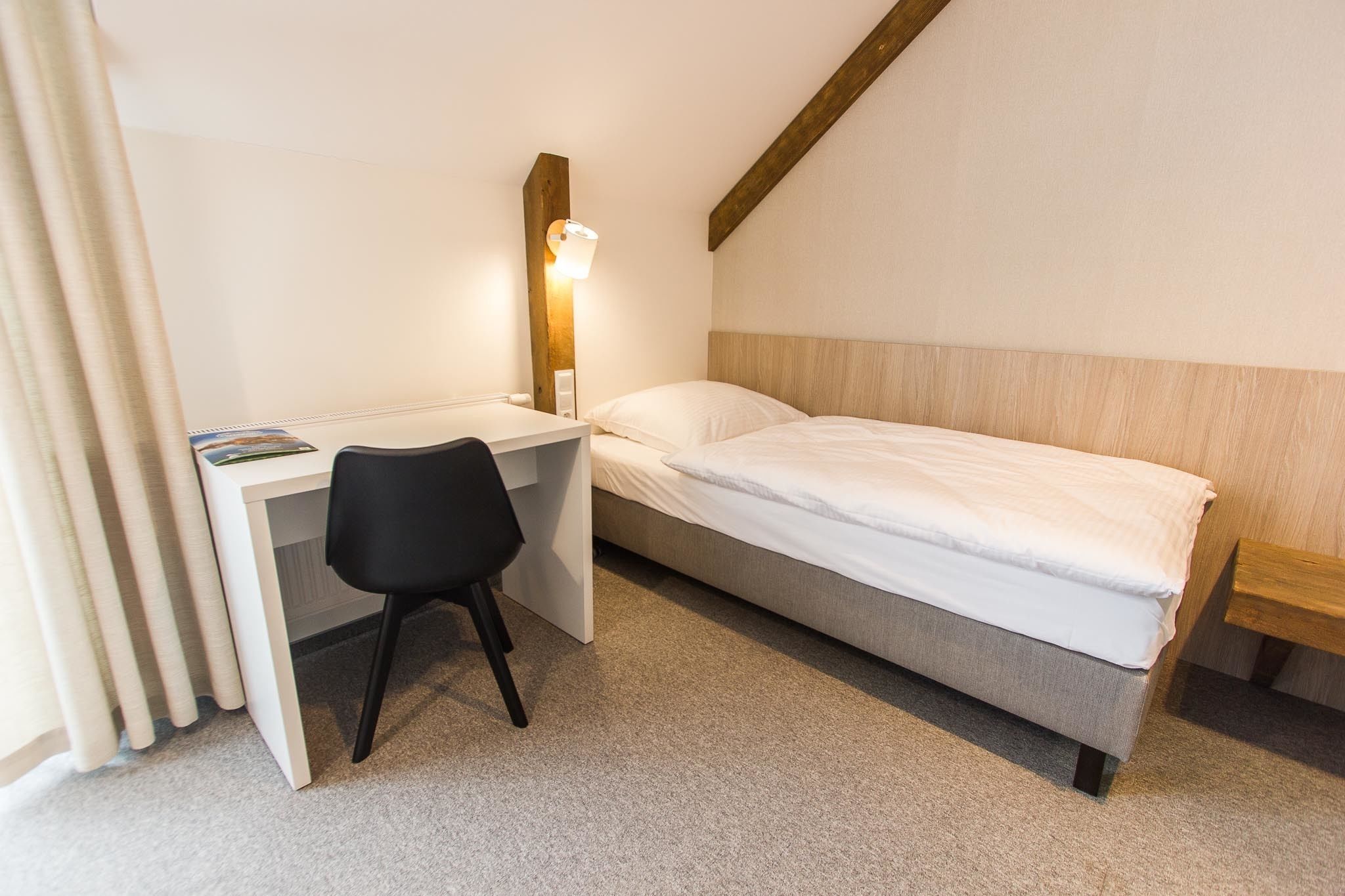 A small, neatly arranged bedroom with a single bed, a desk, and a chair.
