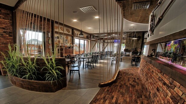 Een ruim restaurant met bakstenen muren, houten tafels en hangplanten.