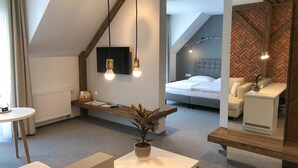 Een moderne hotelkamer met een loft-stijl inrichting, met een bed, een zithoek met een plant en een kleine tafel.