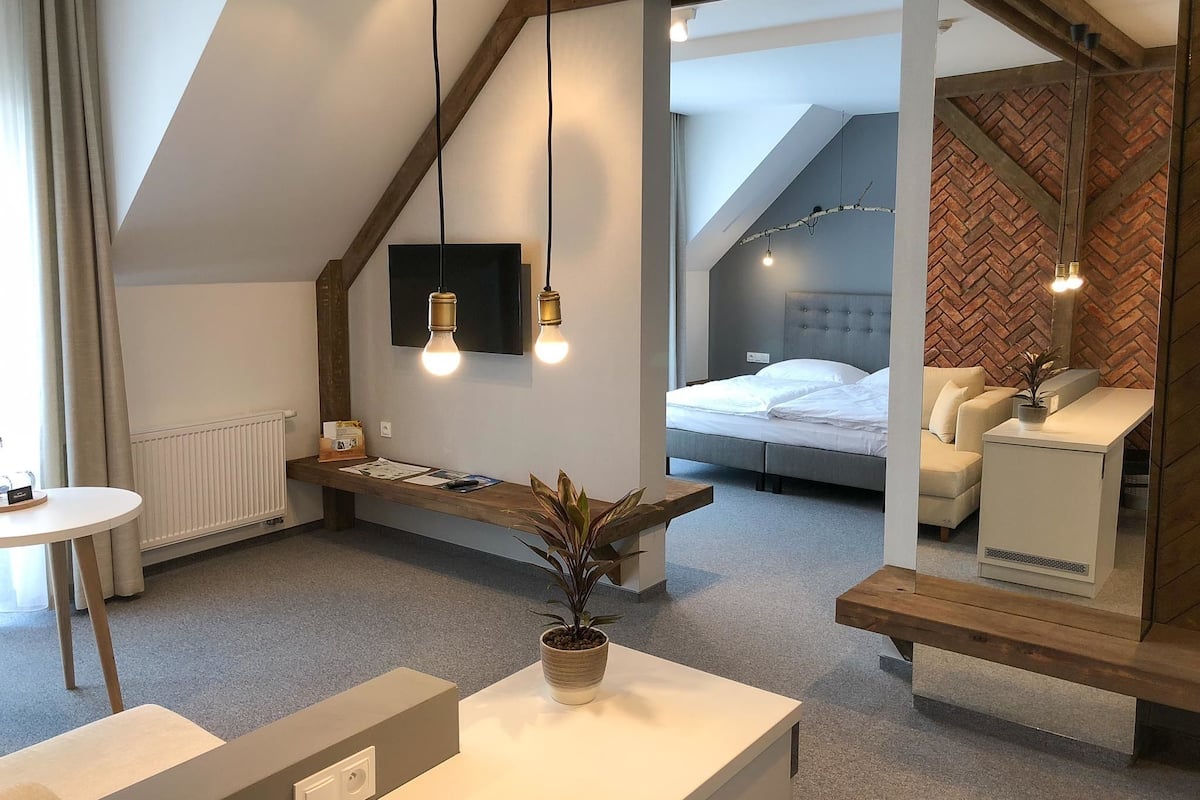 Habitación de hotel moderna con diseño tipo loft, que incluye una cama, una zona de estar con una planta y una pequeña mesa.