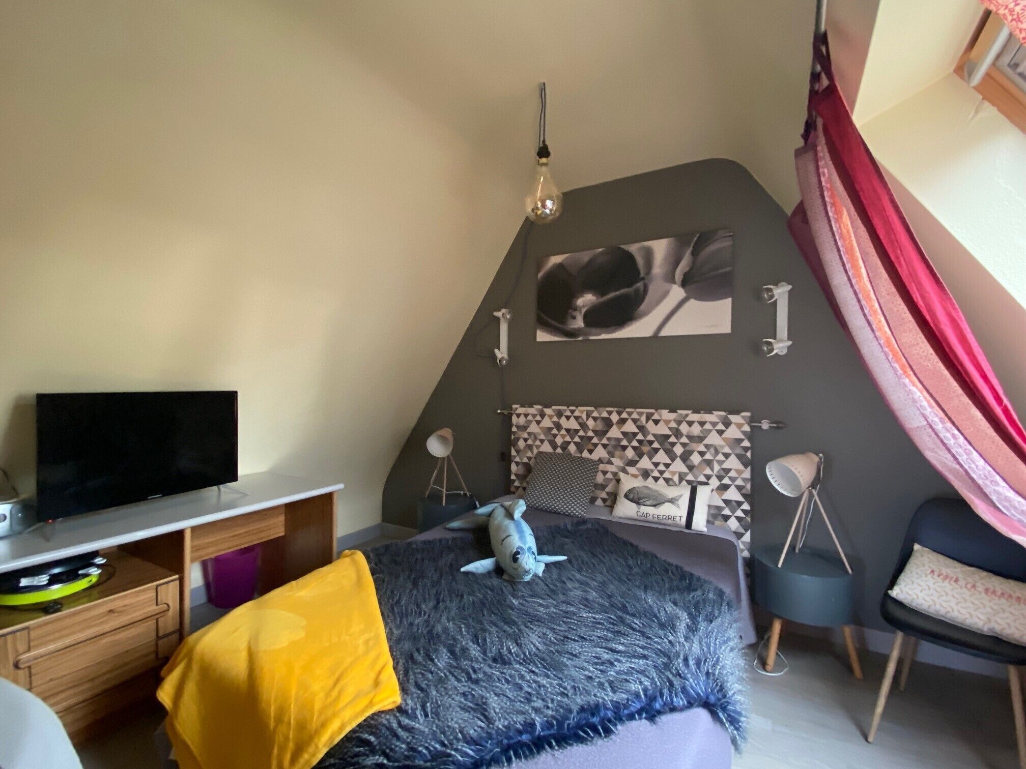 A bedroom with a bed, a desk with a TV, a lamp, and a picture on the wall.