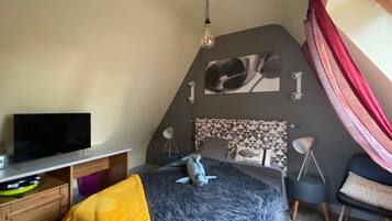 A bedroom with a bed, a desk with a TV, a lamp, and a picture on the wall.