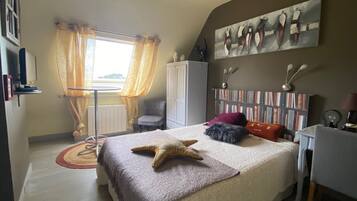 Een slaapkamer met een bed, een bureau, een stoel, een kledingkast en een raam met gordijnen.