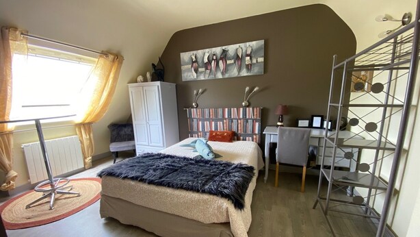 A bedroom with a bed, a desk, a radiator, a wardrobe, and a painting on the wall.