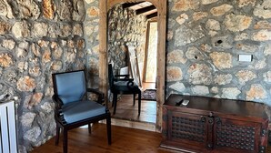 Une pièce aux murs de pierre, avec une chaise en bois, un meuble en bois et un radiateur.