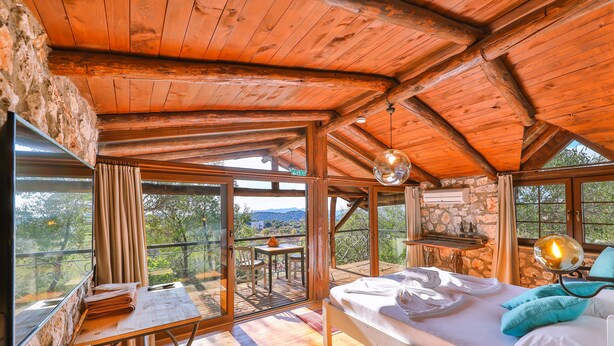 Une cabane en bois avec un lit, une table et une cheminée en pierre.