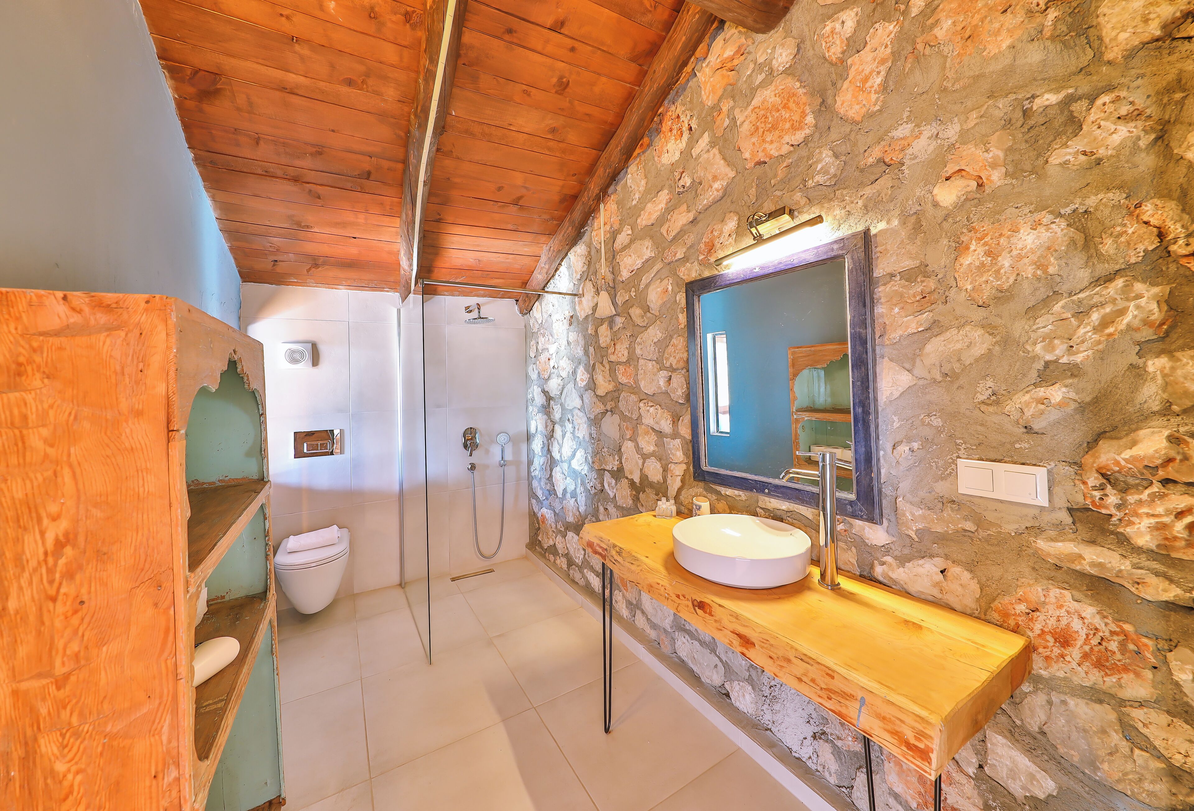 A bathroom with a stone wall, wooden ceiling, and a wooden vanity with a sink.