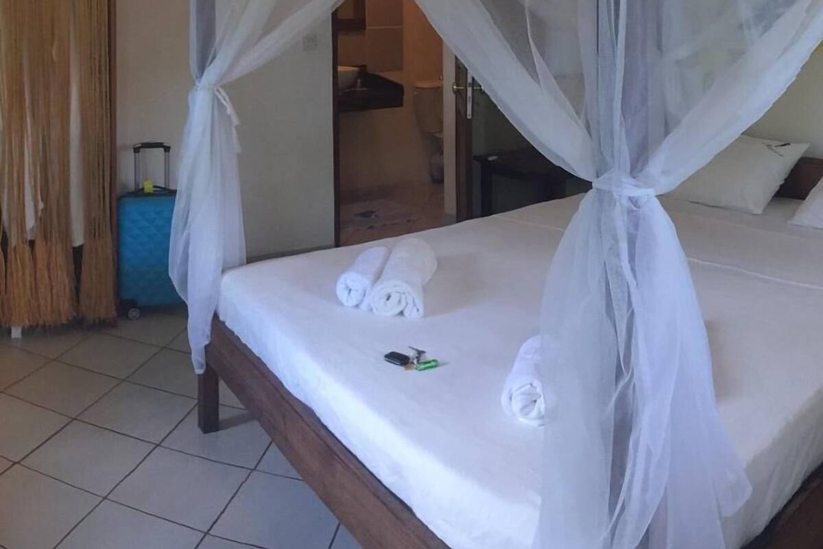 A bed with a canopy, a suitcase, and a bathroom visible in the background.