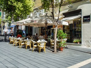 An outdoor cafe with wicker chairs and tables, umbrellas, and potted plants. - Toledo Stay OK (Naples)